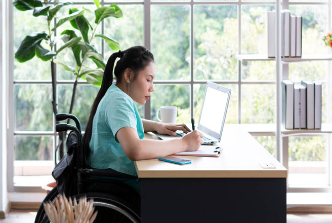 Una chica en silla de ruedas trabaja con su ordenador en un escritorio.
